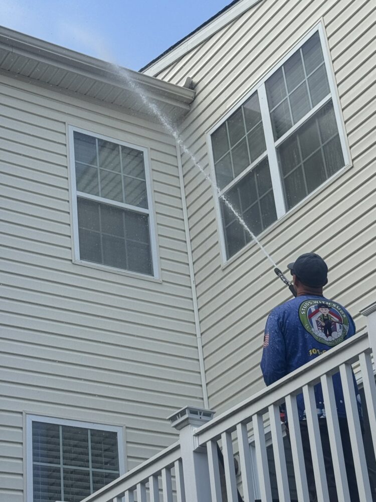 Studs With Suds crew member soft washing house siding from a deck