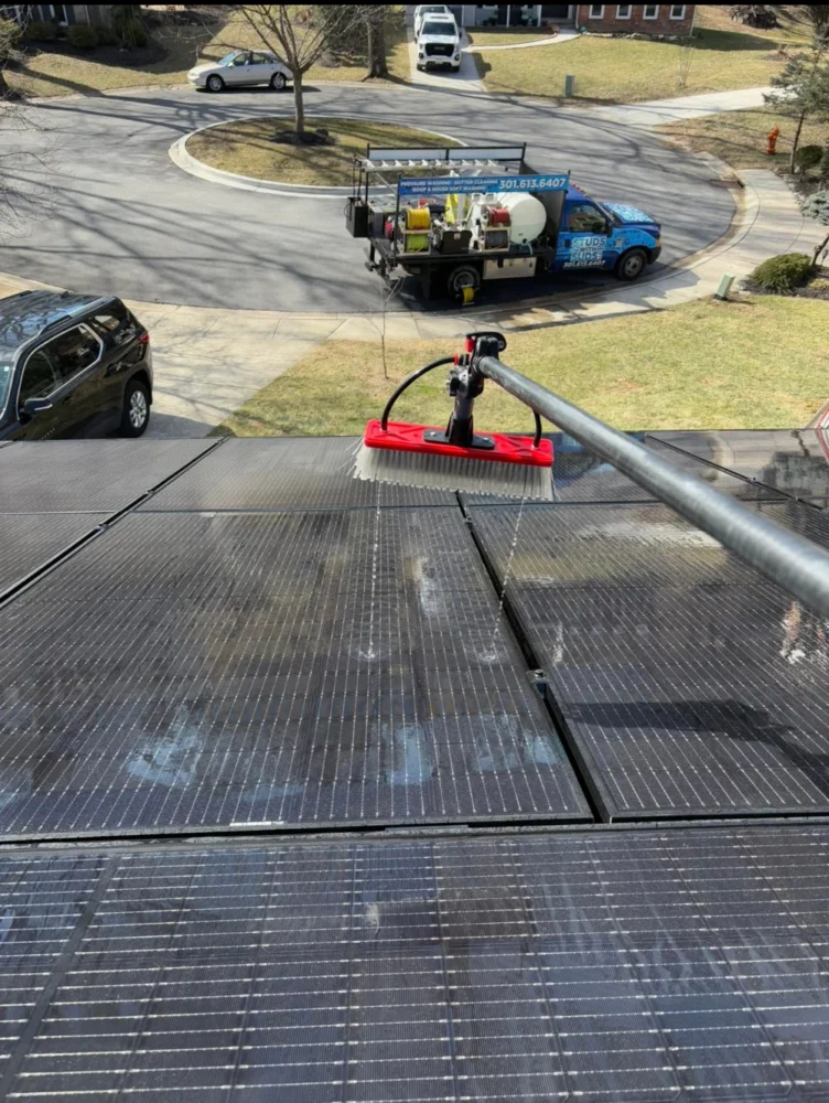 Solar panel cleaning with a brush, with the Studs With Suds truck behind the panels.